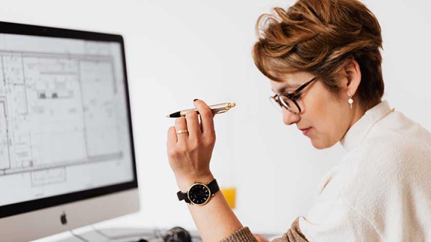 A woman with glasses is sitting in front of a computer and holding a pen. 