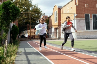 Two smiling tween girls run on a track