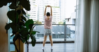 Woman with short hair stands on balcony and stretches her arms above her head